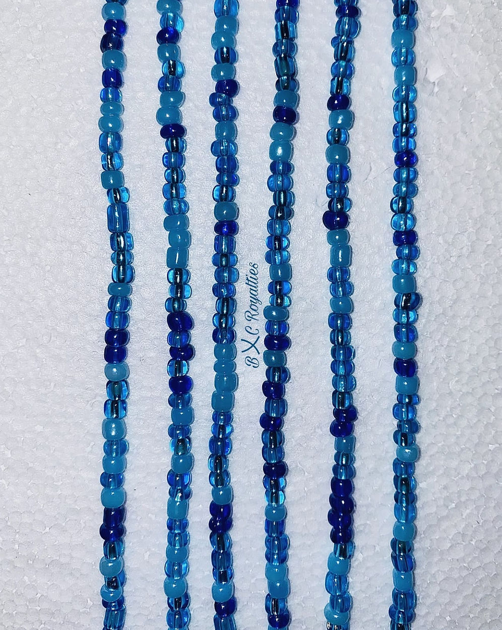Multiple strands of blue beaded necklaces on a textured white background