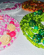 Colorful beaded waist-beads with floral designs on a white background, featuring the brand 'BXC Royalties'.