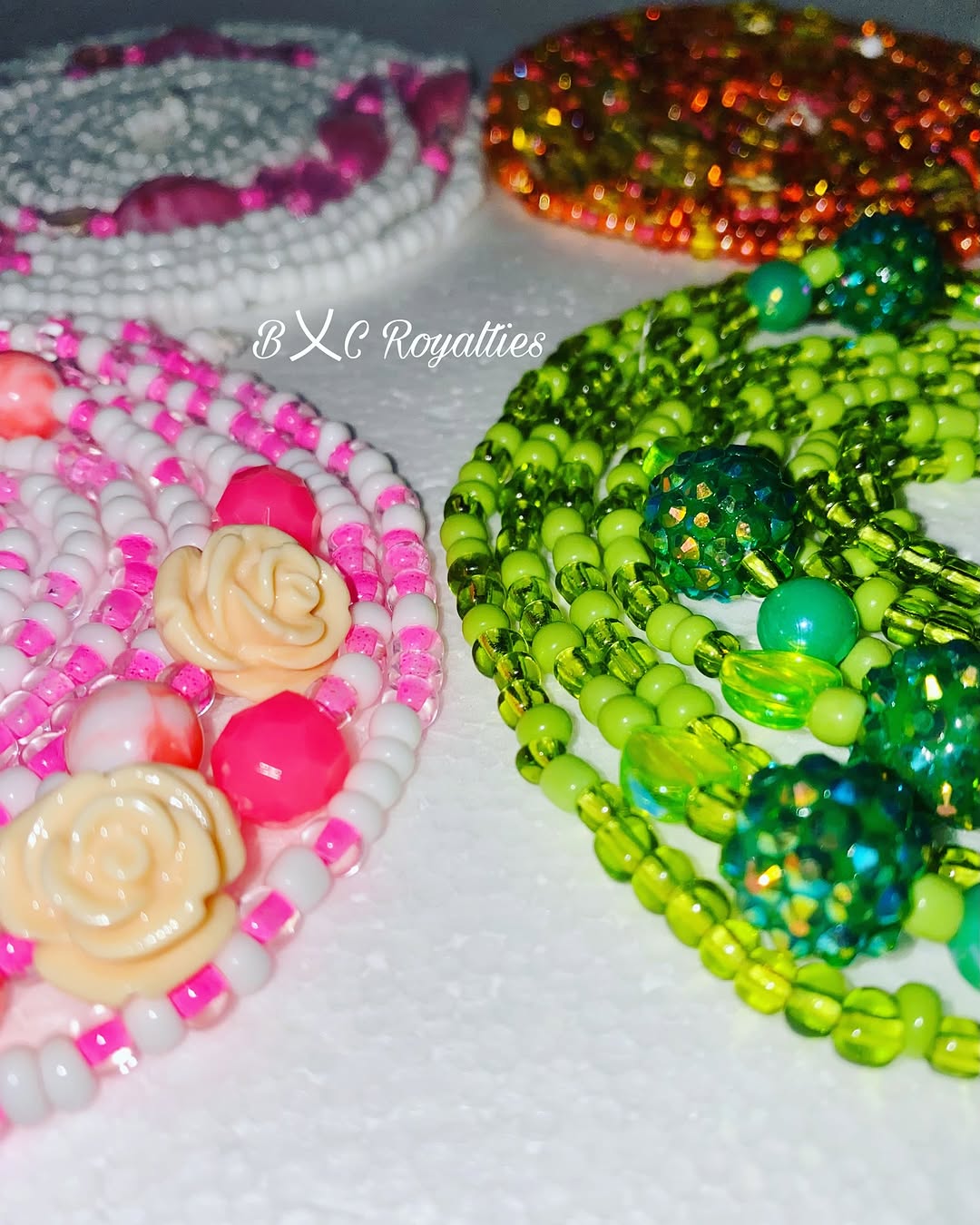 Colorful beaded waist-beads with floral designs on a white background, featuring the brand 'BXC Royalties'.