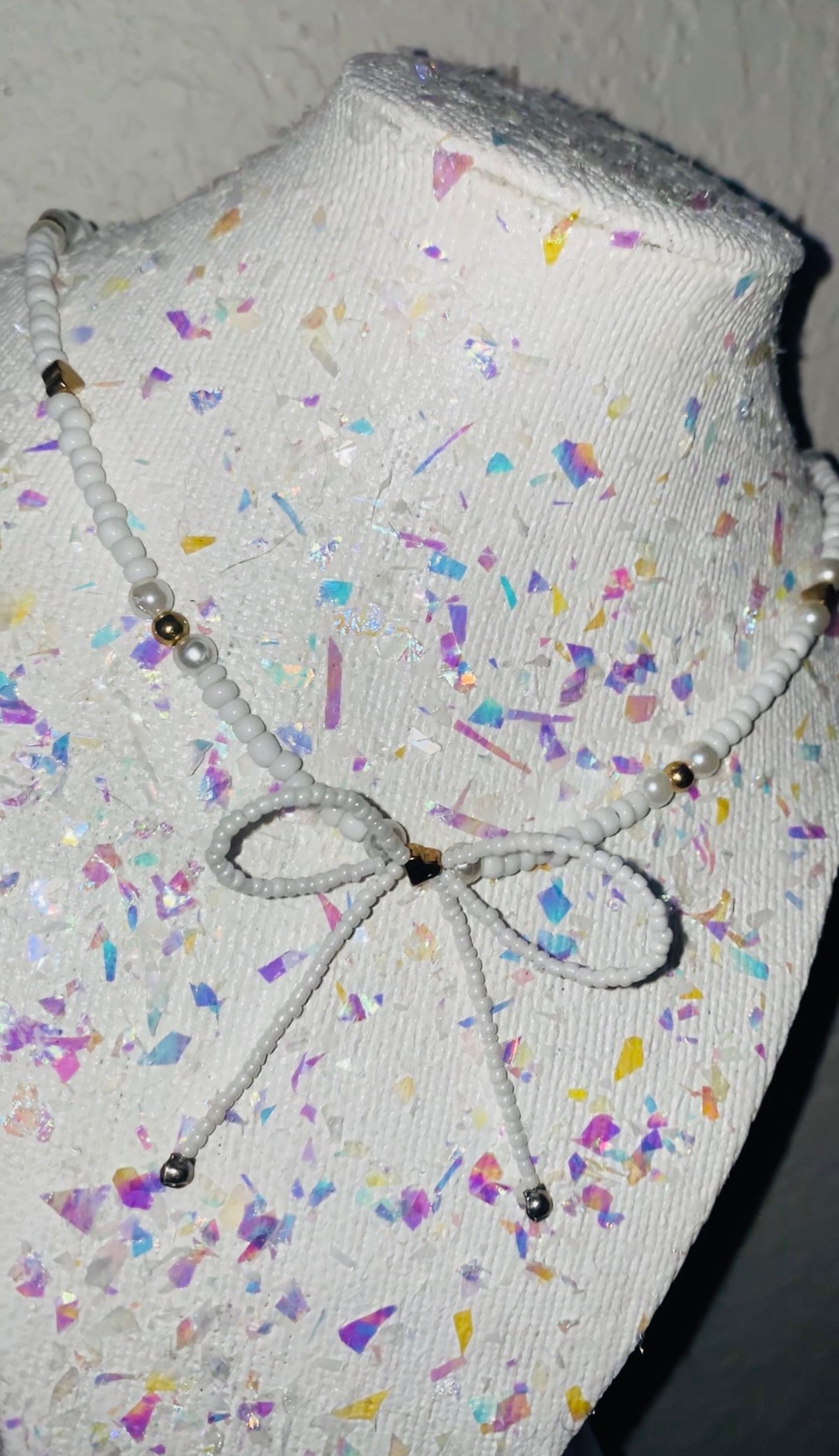 Mannequin head with colorful confetti pattern and decorative bow on a plain background