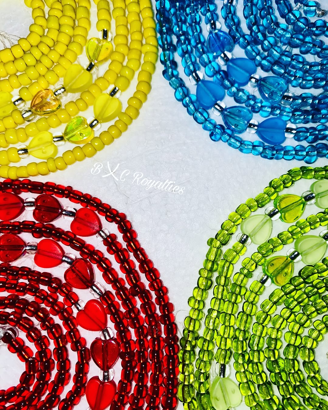 Four colorful beaded necklaces in yellow, blue, red, and green on a white background.