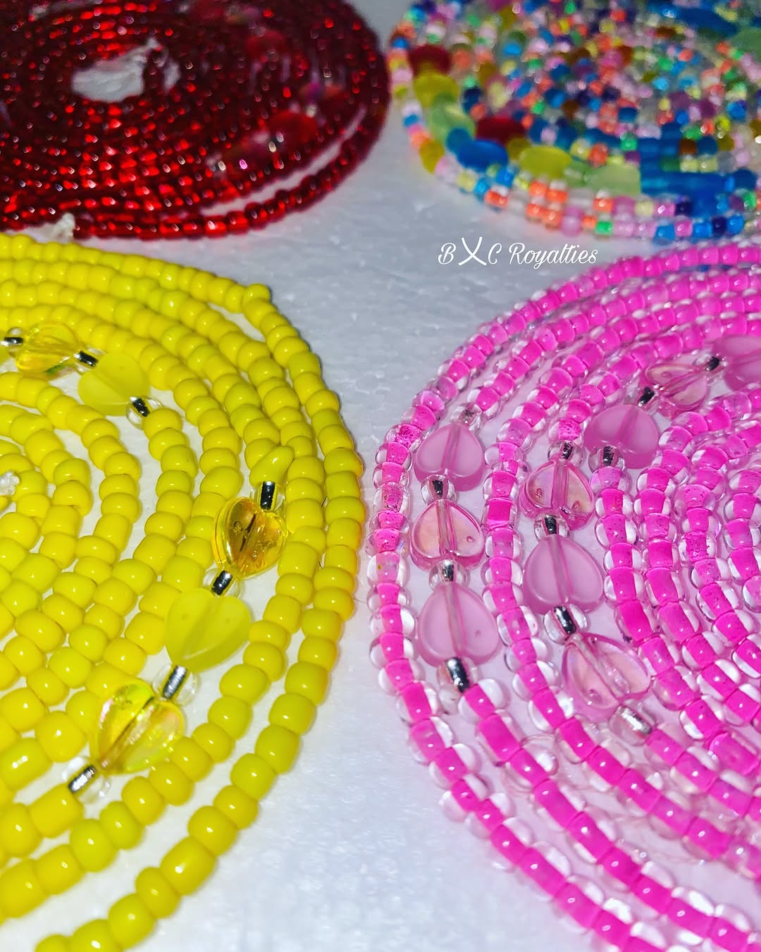 Colorful beaded necklaces on a white surface with 'BXC Royalties' branding.
