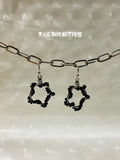 Black star-shaped earrings hanging from a chain against a neutral background with 'BxC Royalties' branding.