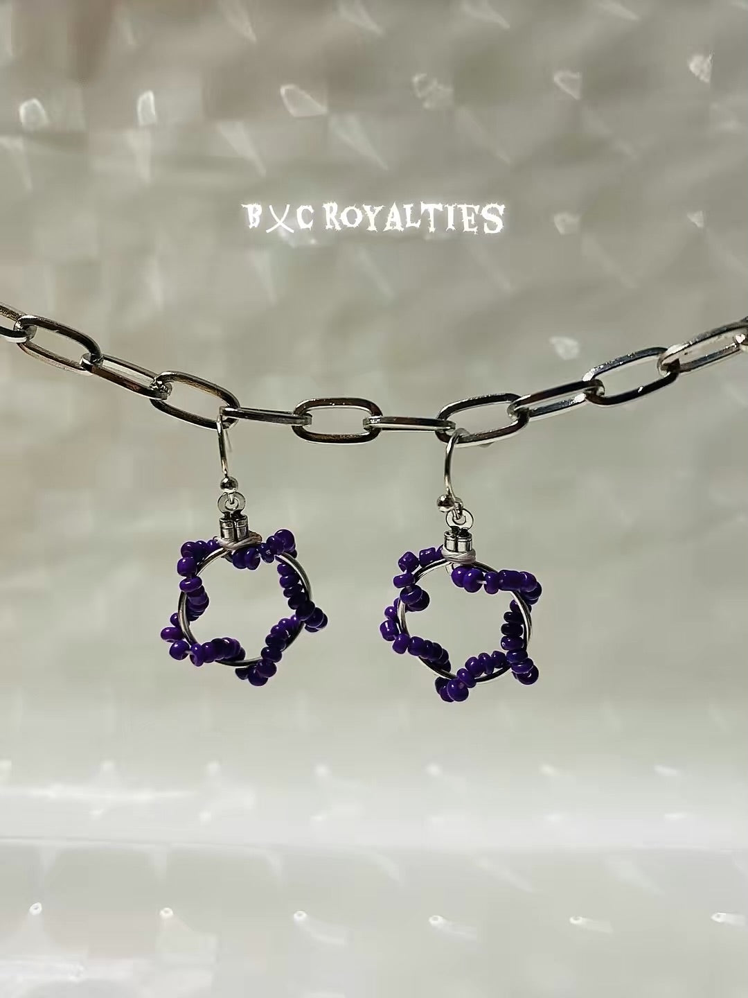 Purple beaded earrings on a silver chain with 'BXC Royalties' branding.