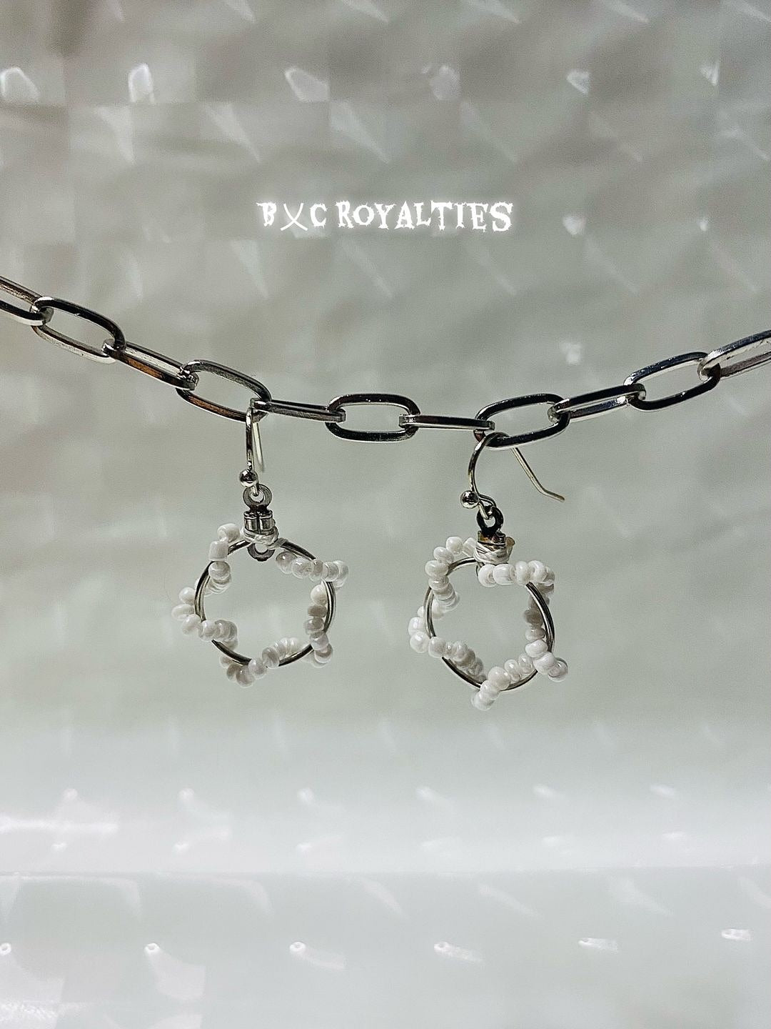Pair of earrings with circular design on a textured surface, featuring the brand 'BXC Royalties'.