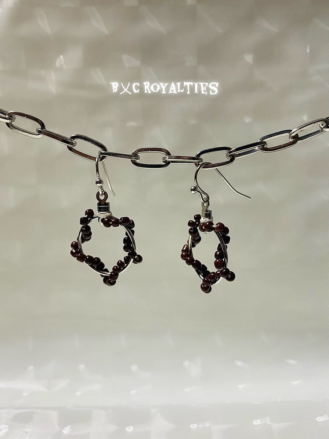 Pair of earrings with dark beads hanging from a silver chain on a light background.