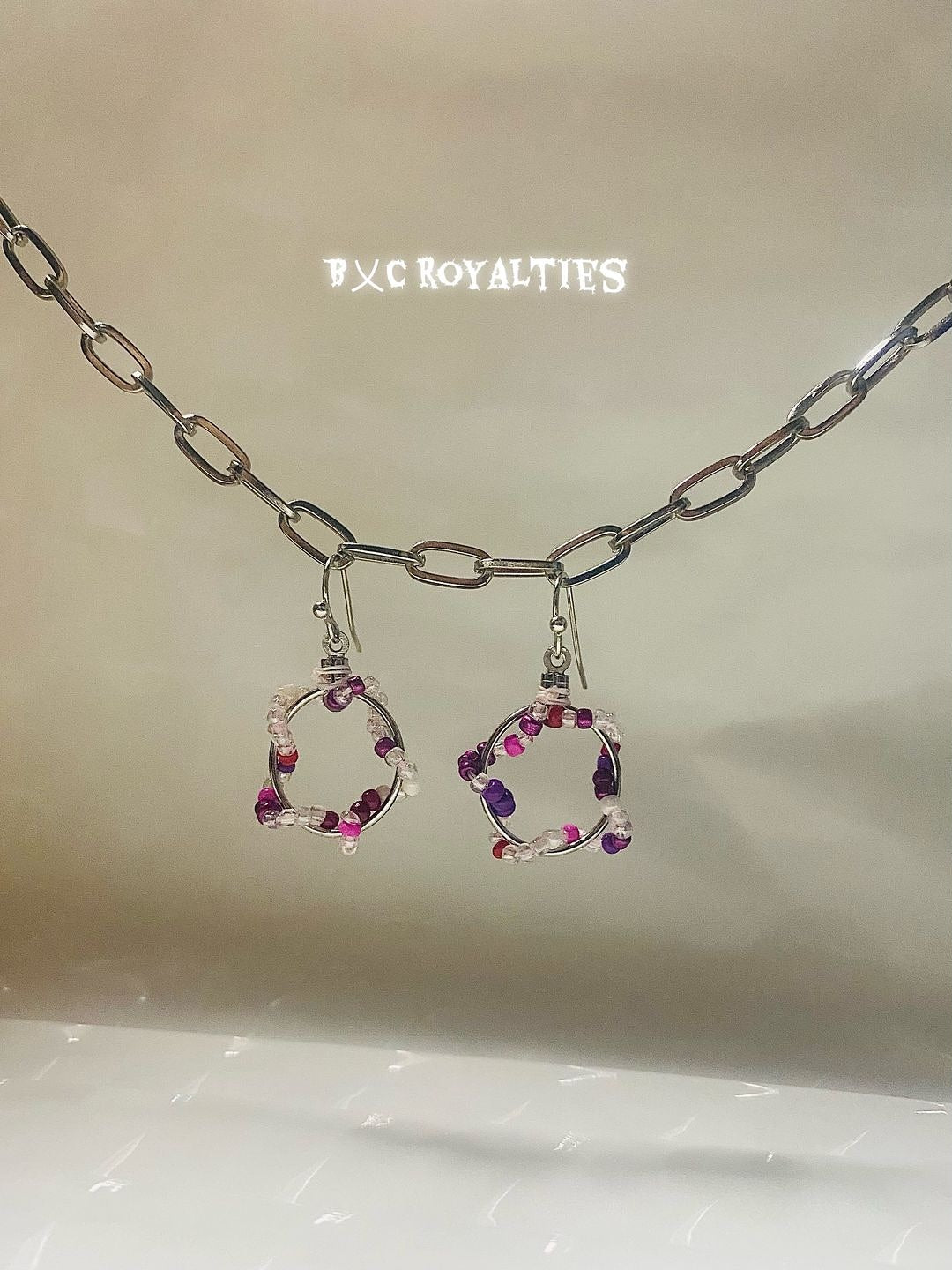 Pair of earrings with circular design and embedded stones, displayed on a chain against a neutral background.
