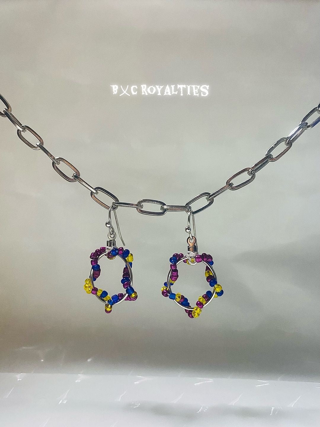 Colorful hoop earrings hanging from a silver chain on a light gray background with 'B&C Royalties' branding.