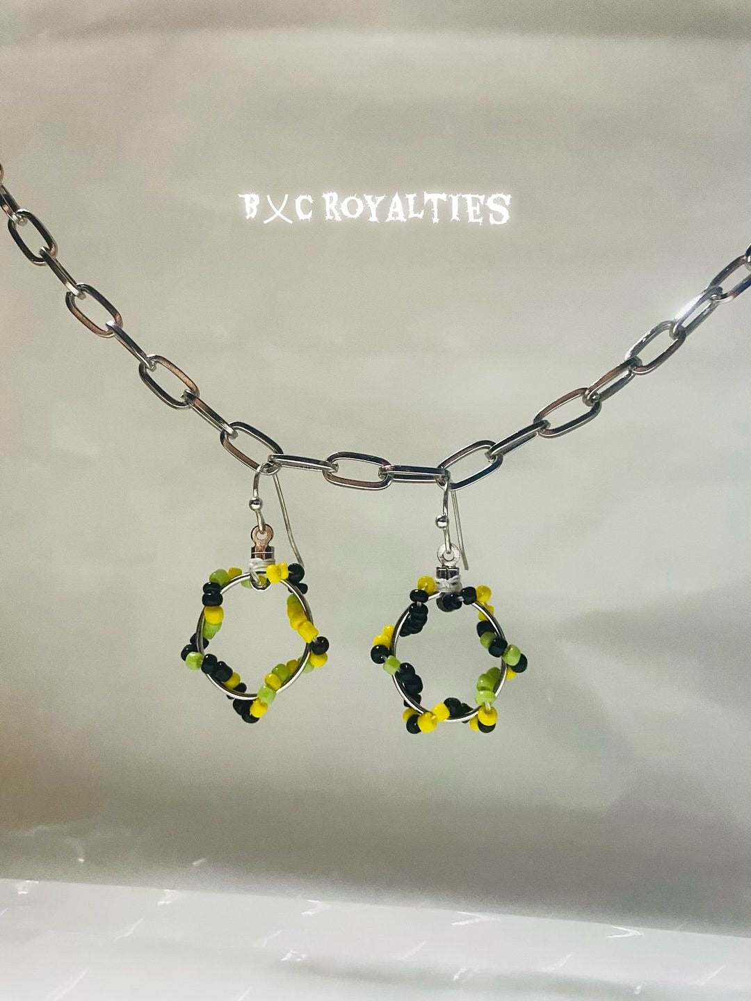 Hexagonal beaded earrings with yellow, lime green  and black accents on a silver chain against a white background.