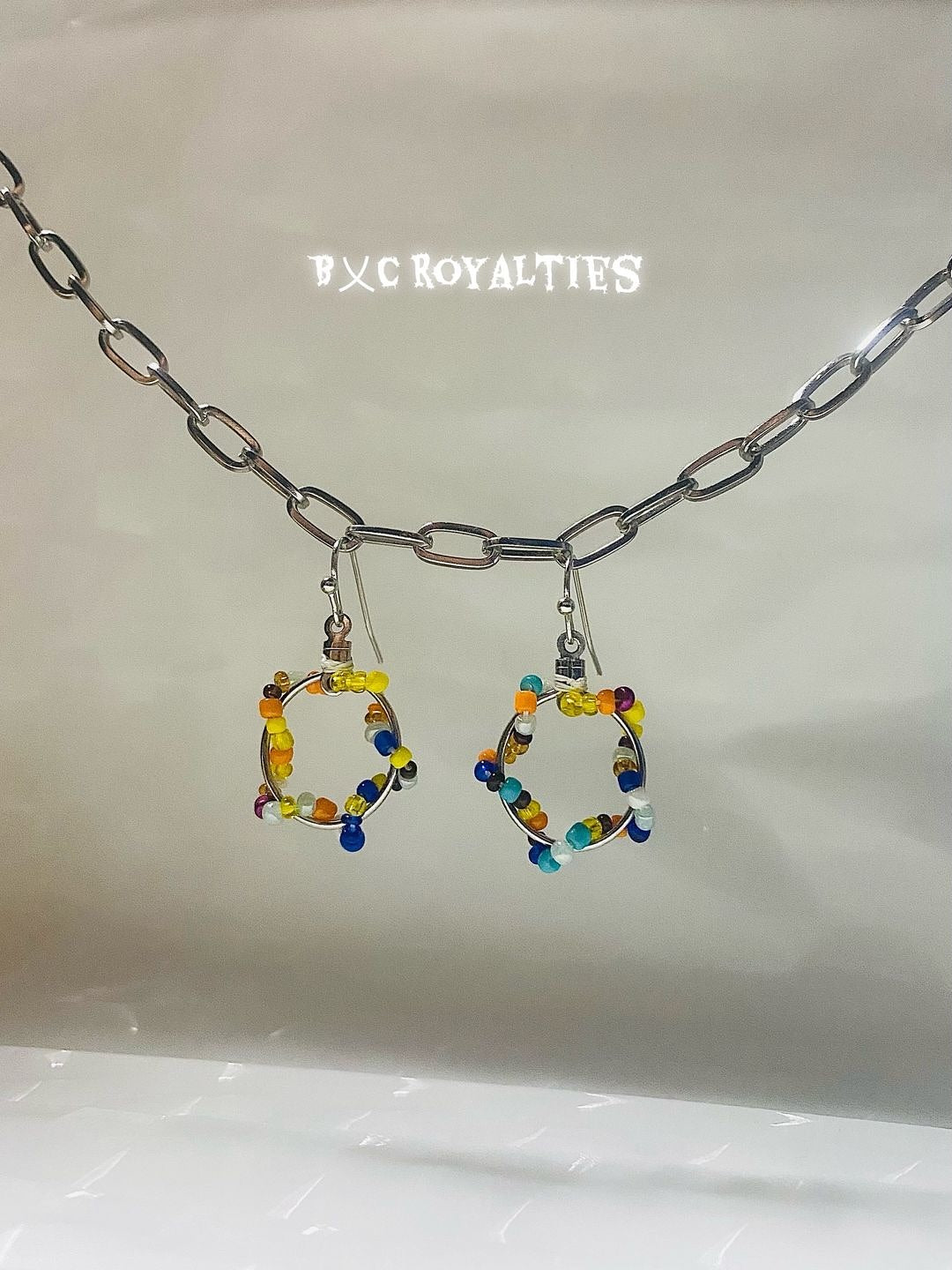 Earrings with colorful beads on a light gray background, branded 'BXC Royalties'.