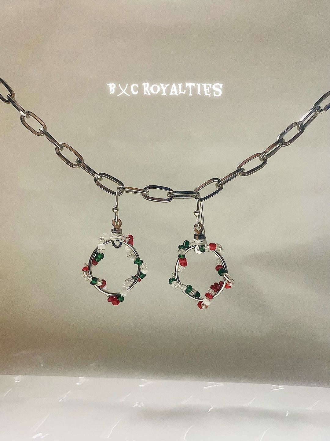 Pair of hoop earrings with floral designs hanging from a chain on a neutral background.