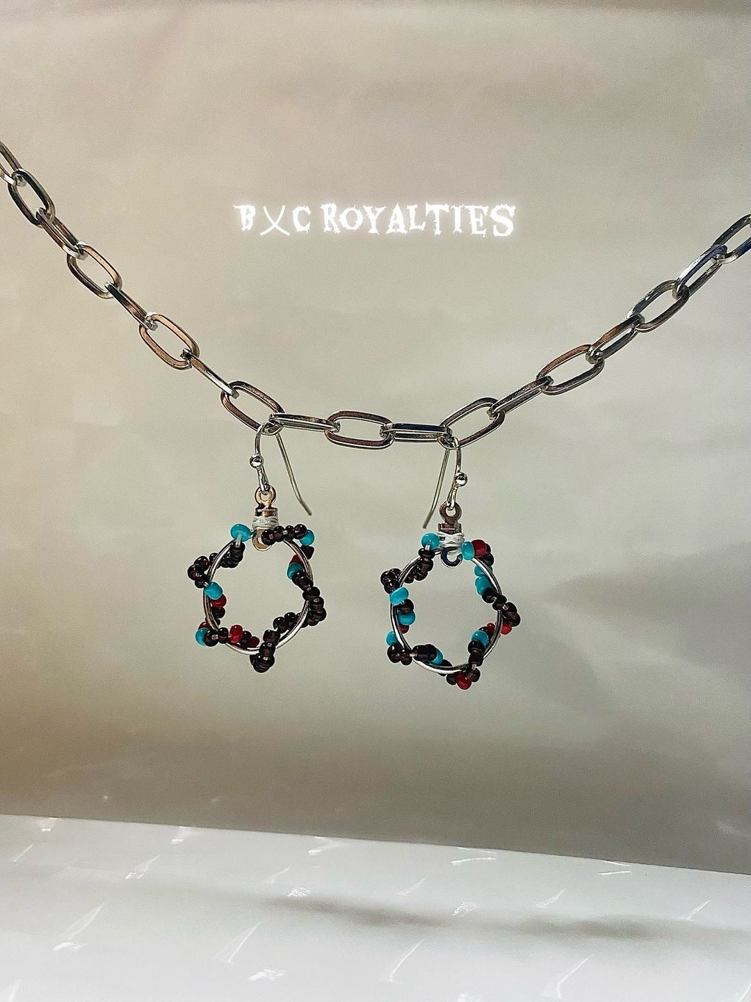 Pair of hexagonal earrings with colorful beads on a chain, branded 'BXC Royalties'.