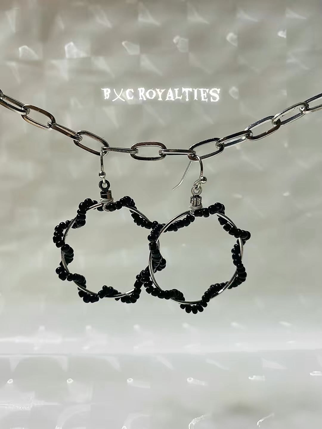 Black hoop earrings with a chain on a textured white background, featuring the brand 'BXC Royalties'.