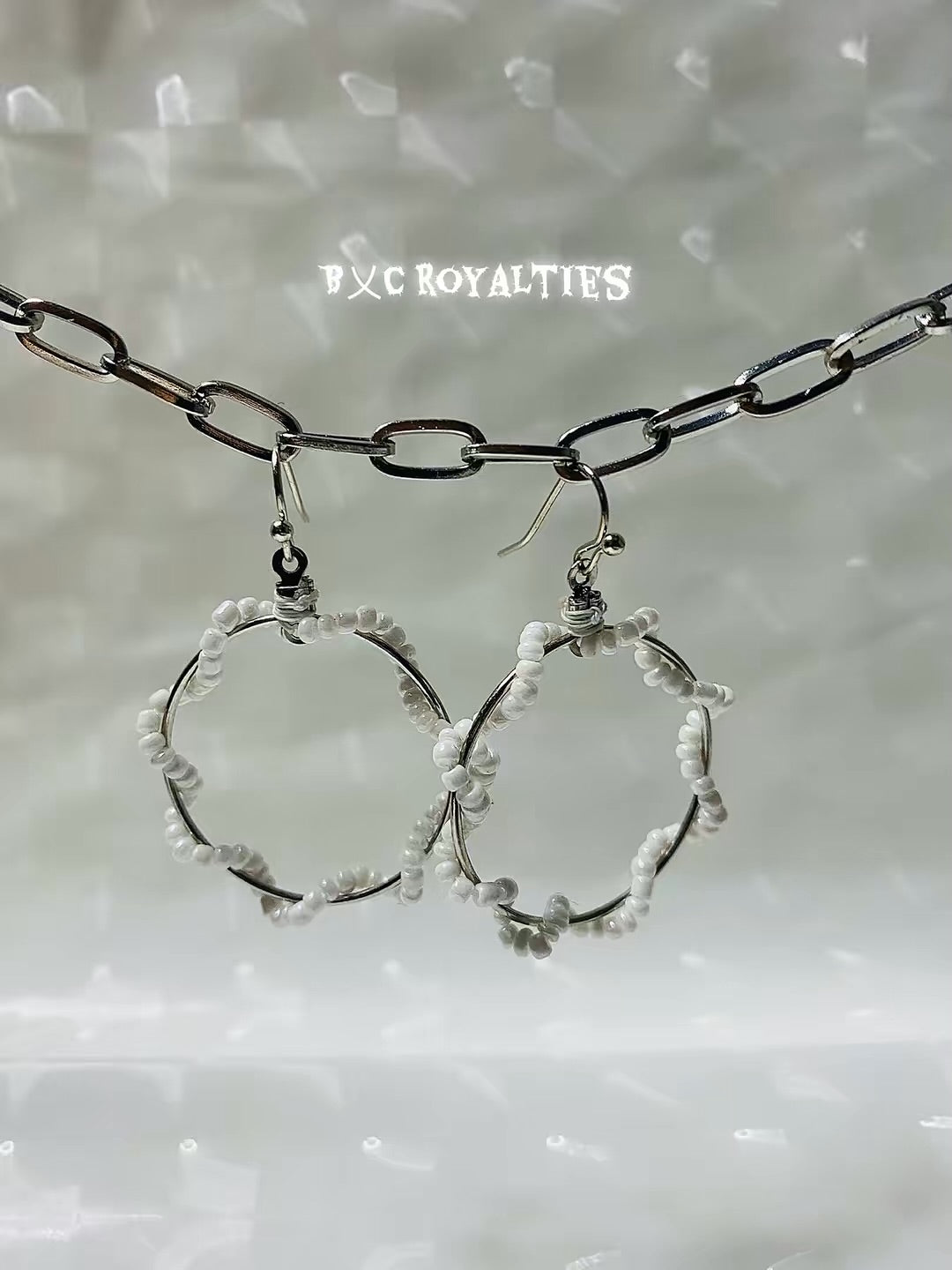 Silver hoop earrings with white beads hanging from a chain against a light background.