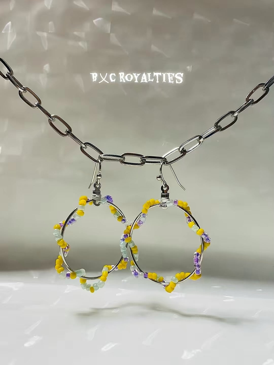 Hoop earrings with yellow and purple beads on a chain against a neutral background