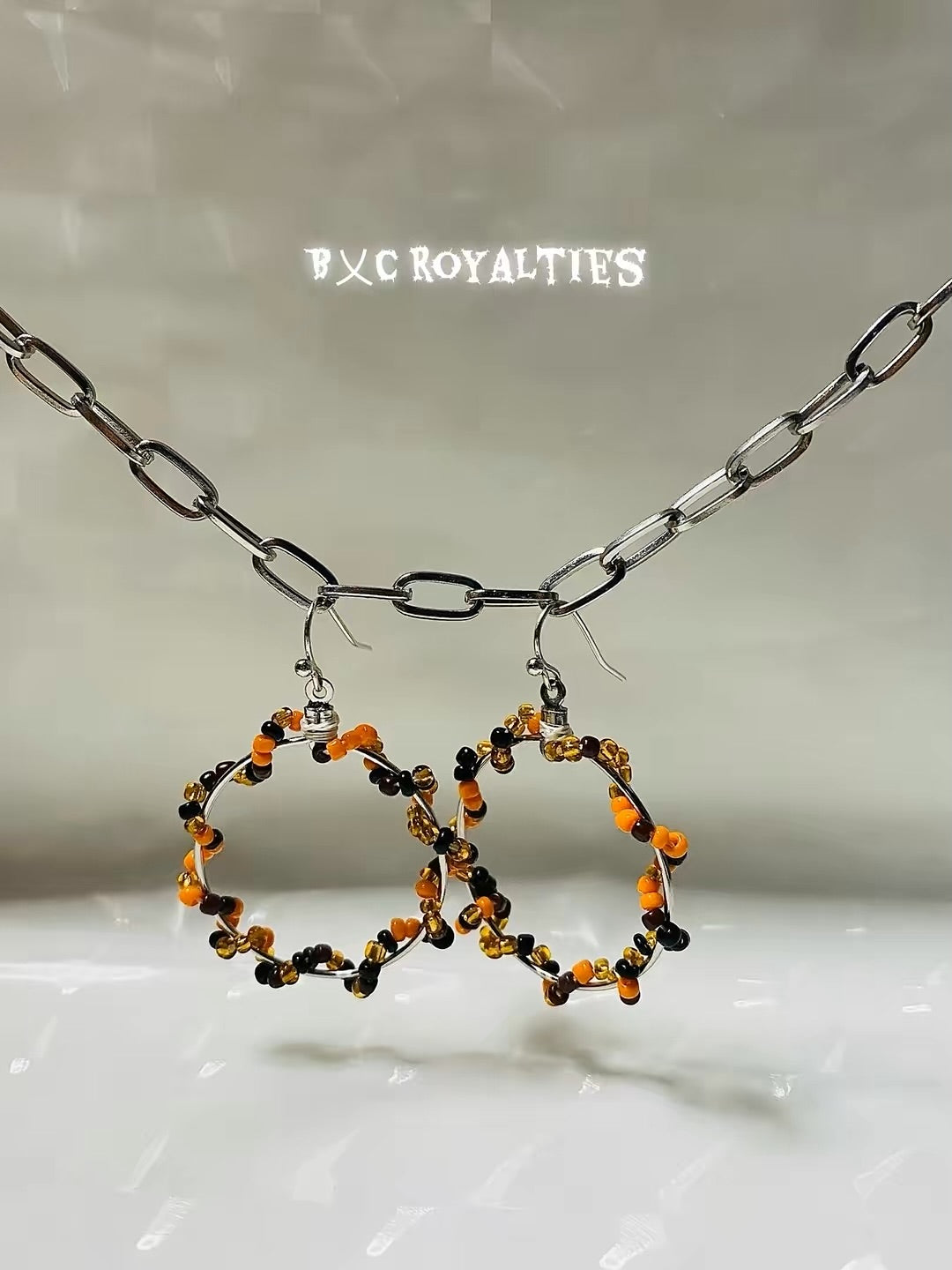 Beaded hoop earrings on a chain against a neutral background with 'BXC Royalties' branding.