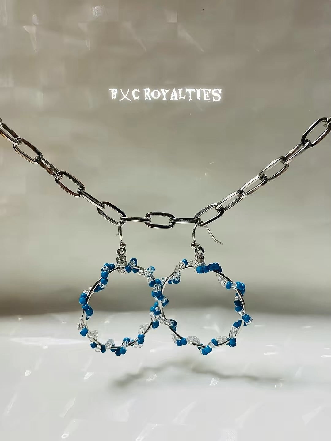 Blue beaded hoop earrings with a silver chain on a light background
