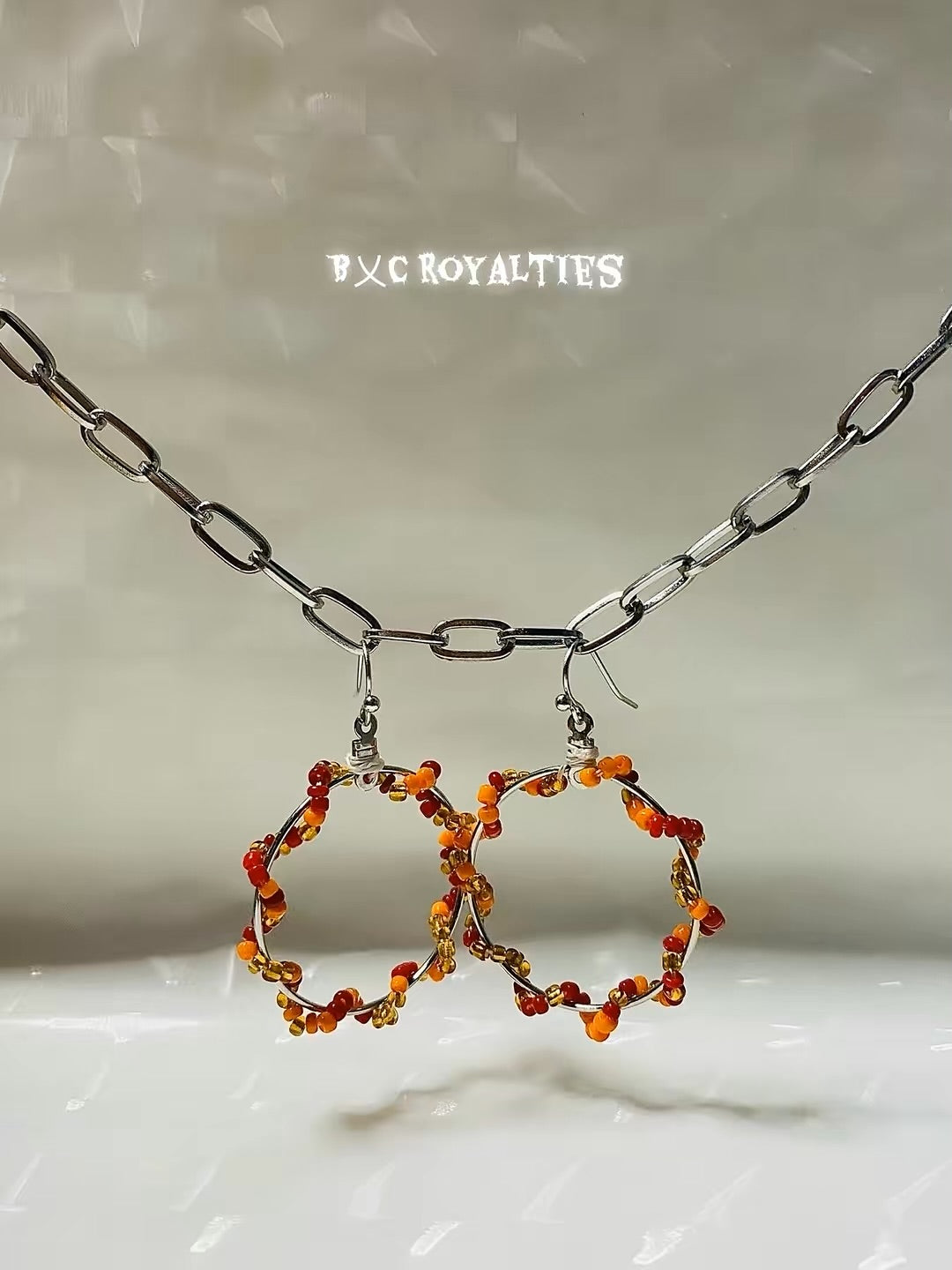 Hoop earrings with orange beads hanging from a chain on a light background
