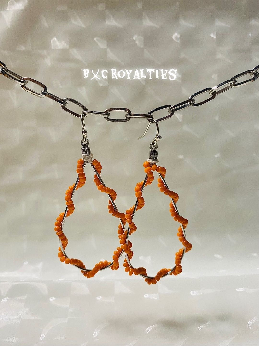 Orange beaded earrings on a textured surface with 'BXC Royalties' branding.