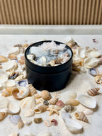 Black bowl with seashells and sand on a bed of seashells and sand