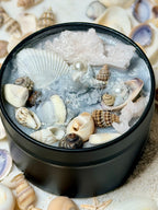 Black container filled with seashells and crystals on a bed of sand