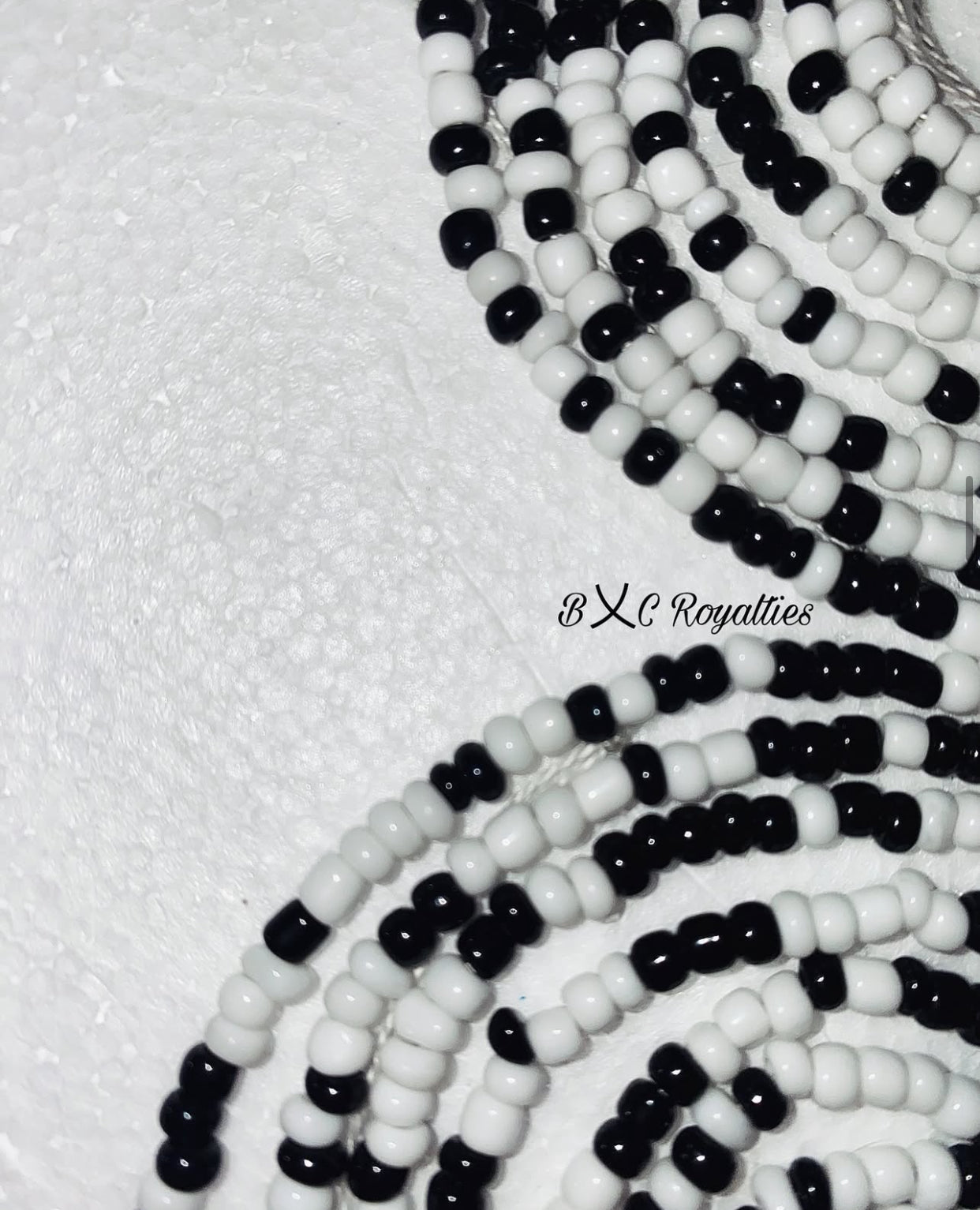 Close-up of black and white beaded strands on a textured white background with 'BXC Royalties' branding.