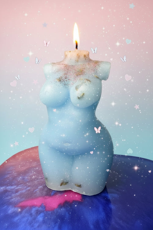 A light blue silicone or rubber female torso-shaped candle with a small white wick at the top, resting on a blue and pink marbled surface against a beige textured wall.