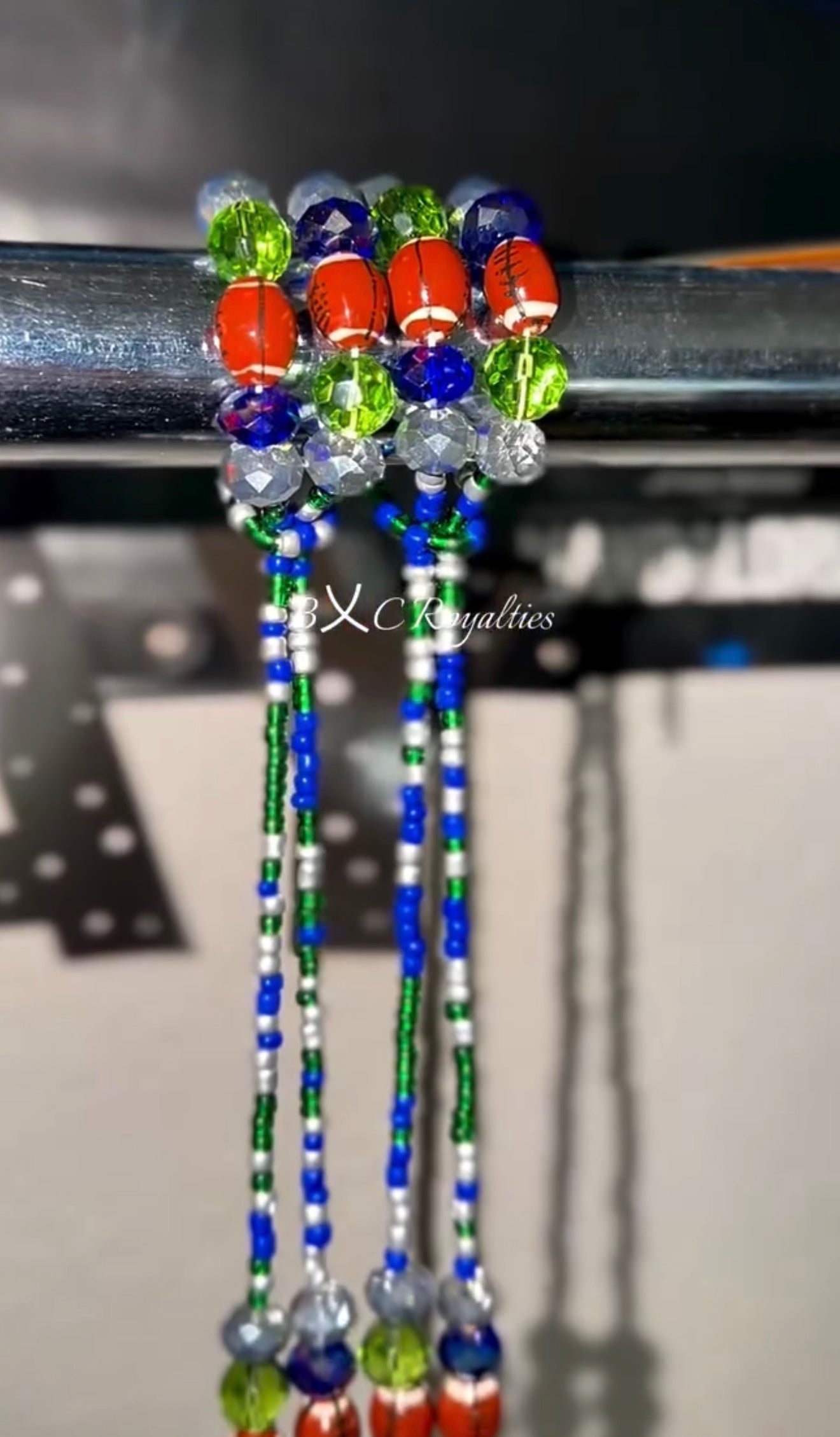 Colorful beaded waist-bead extensions on a metal rod with a blurred background.