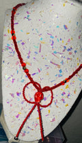 Red beaded necklace on a textured surface with colorful confetti-like pattern