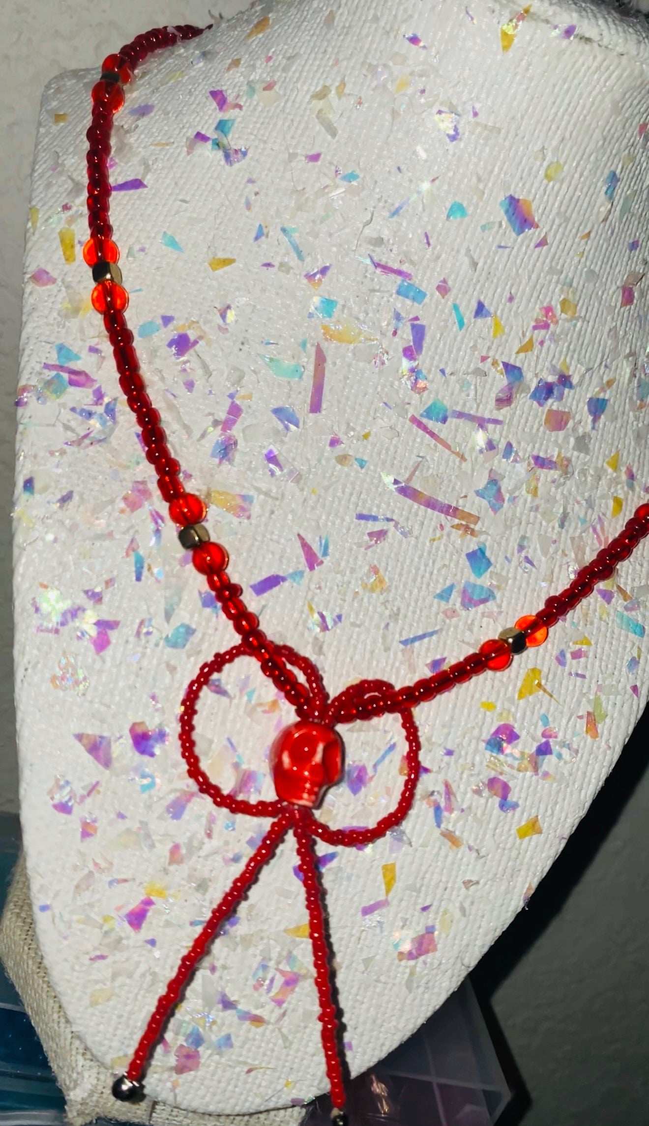 Red beaded necklace on a textured surface with colorful confetti-like pattern
