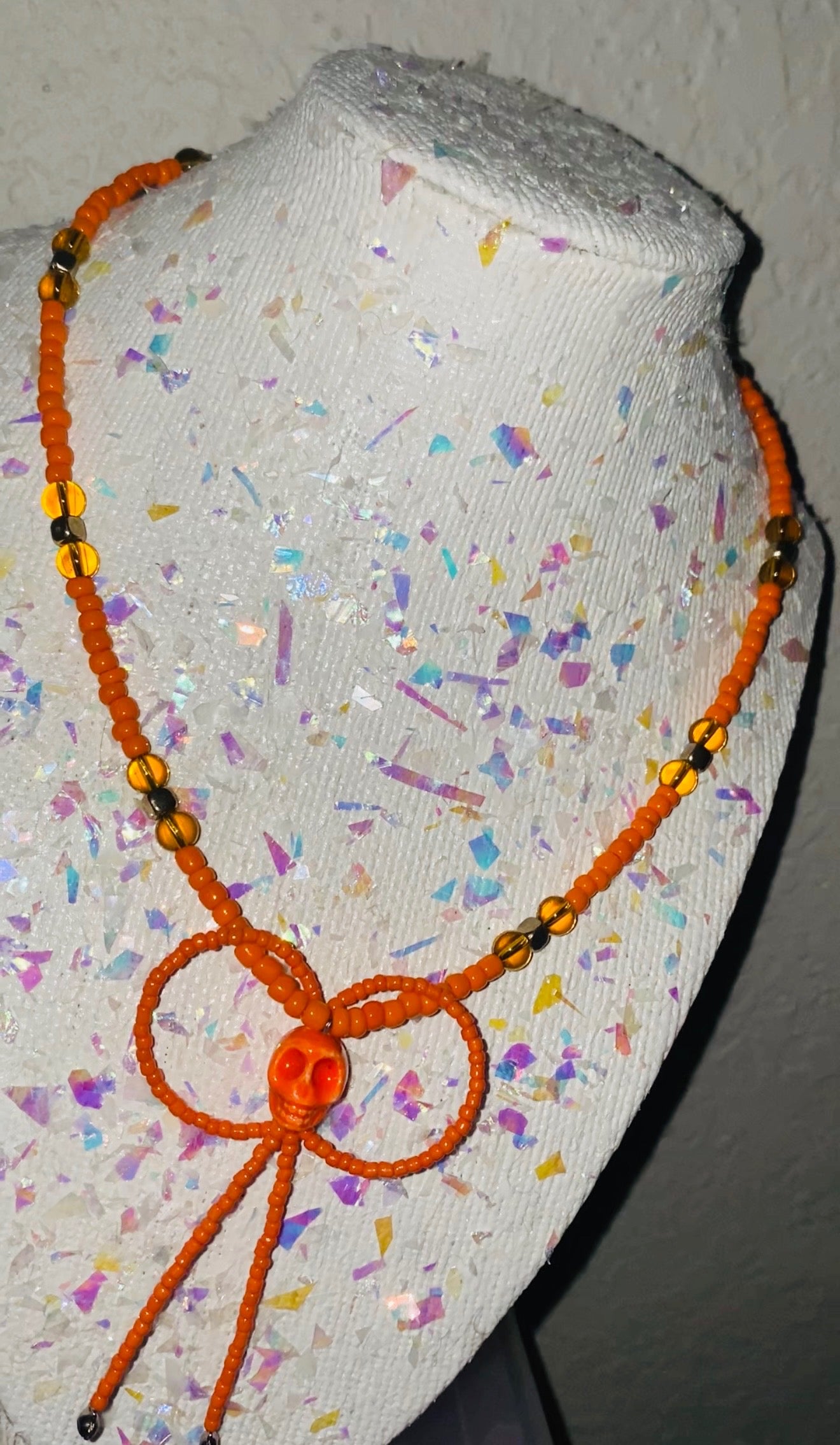 Orange beaded necklace on a mannequin head with colorful confetti background