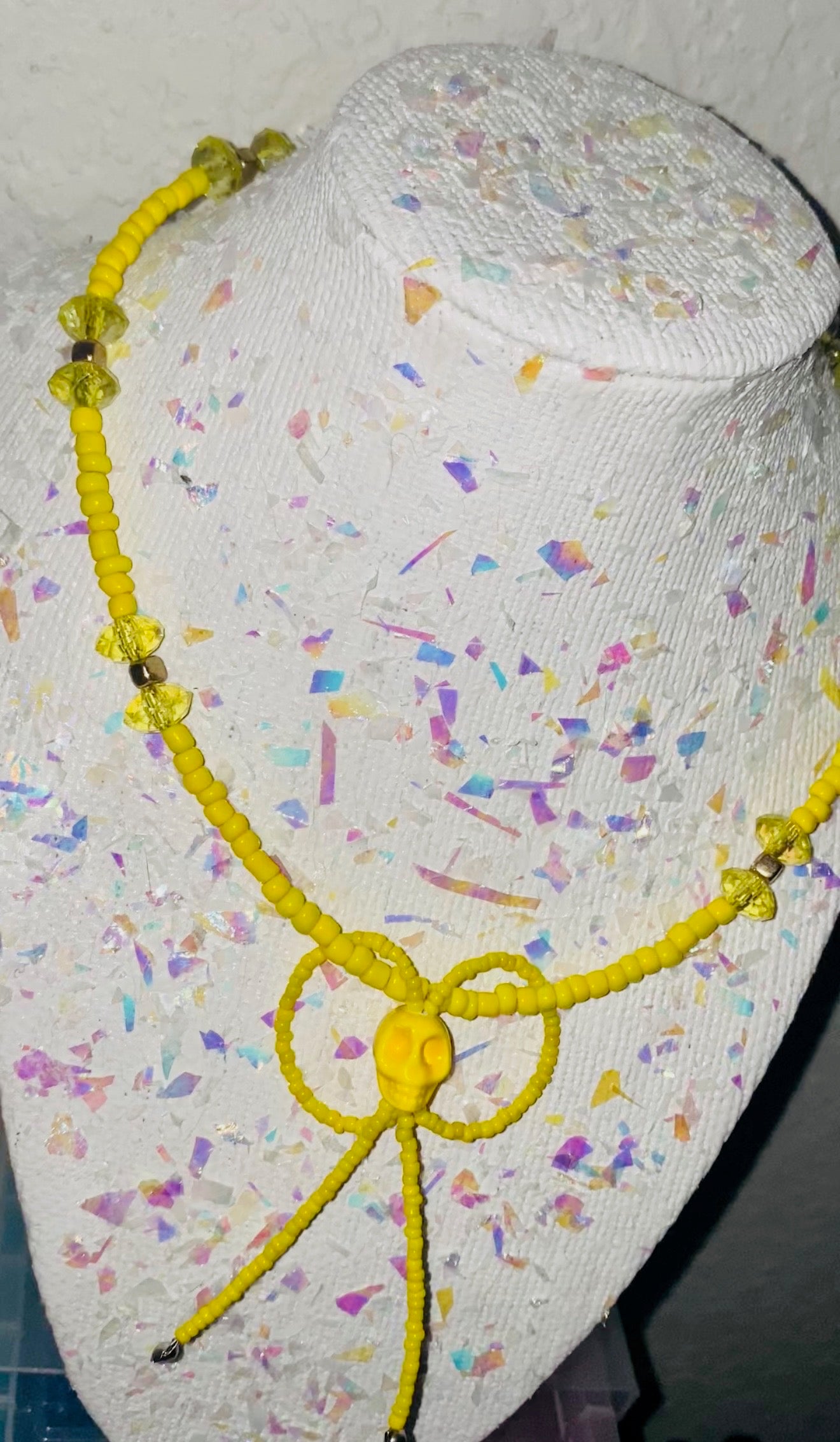 Yellow necklace on a mannequin head with a colorful, confetti-like background