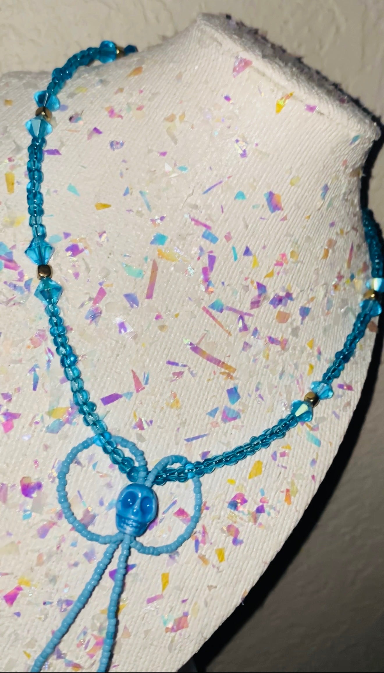 Blue beaded necklace on a textured surface with colorful confetti