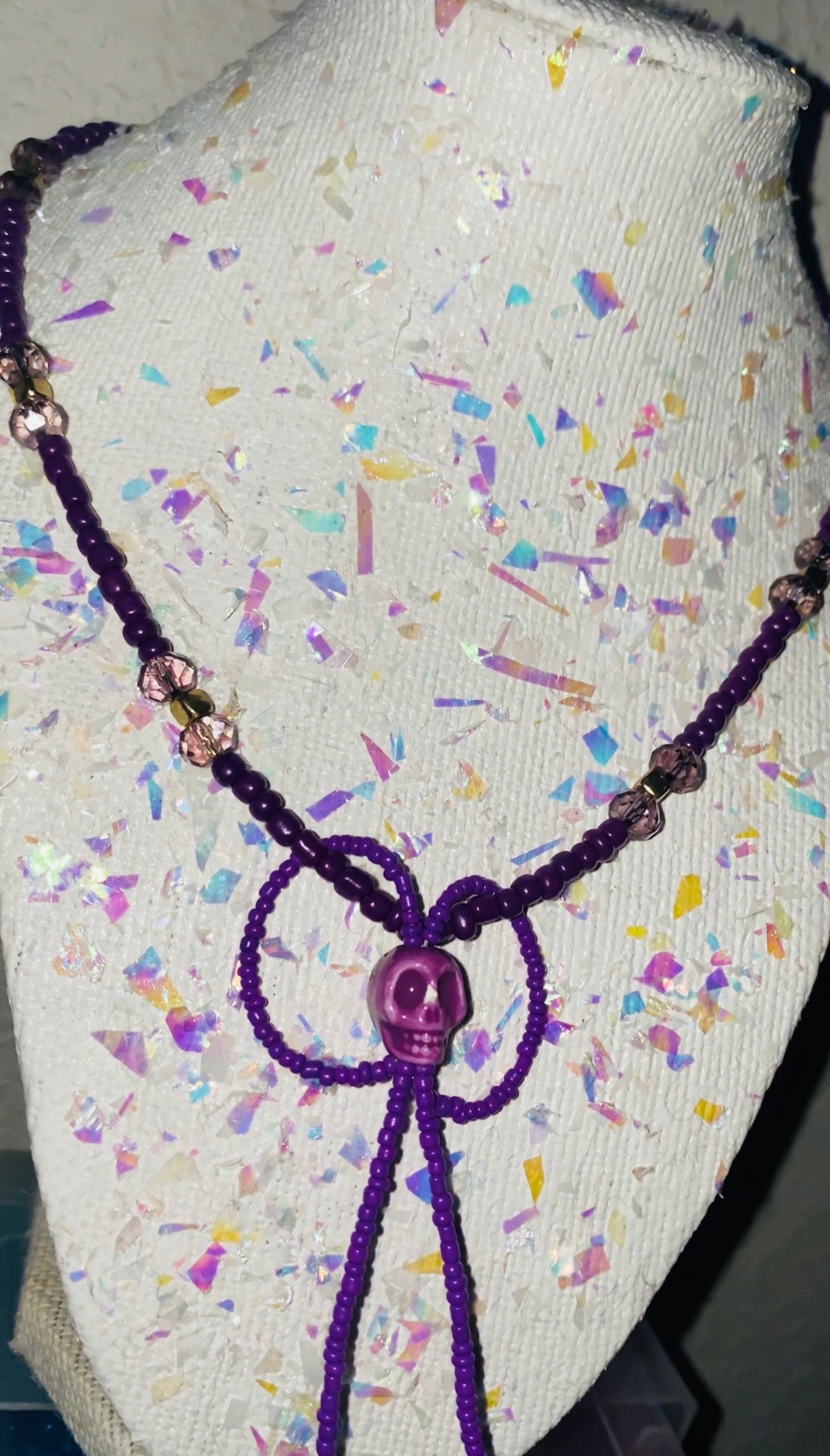 Purple beaded necklace on a mannequin head with a colorful confetti background