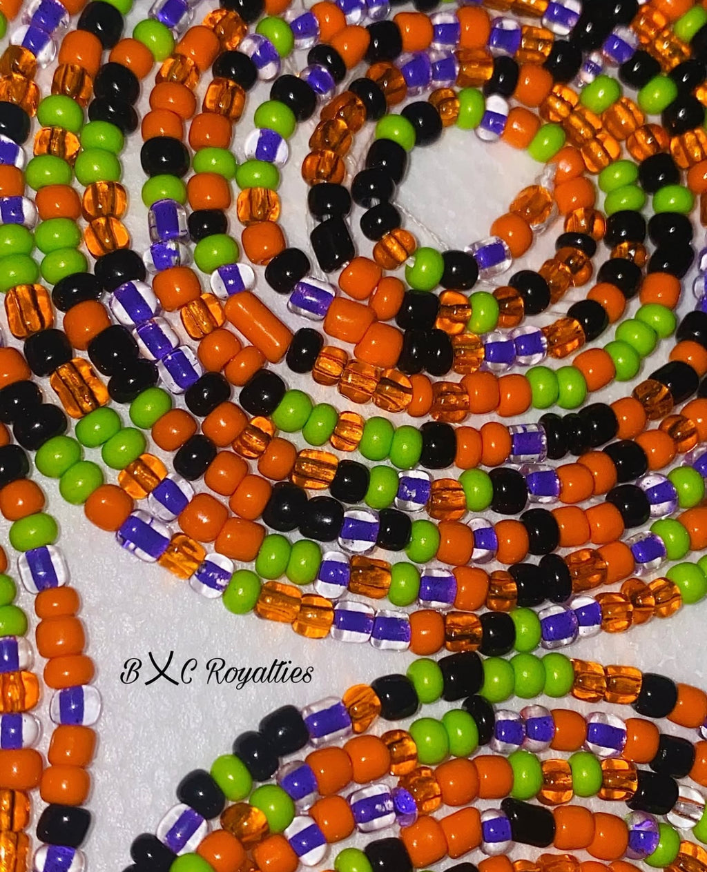 Close-up of colorful beaded strands in orange, green, and black on a white background.