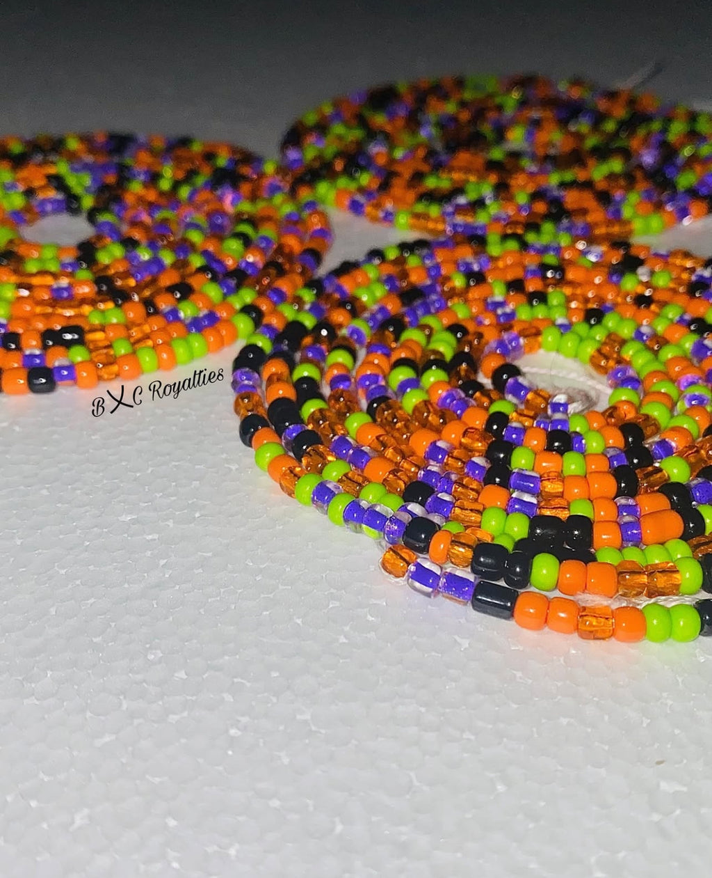 Colorful beaded necklace with orange, green, and black beads on a gray background.