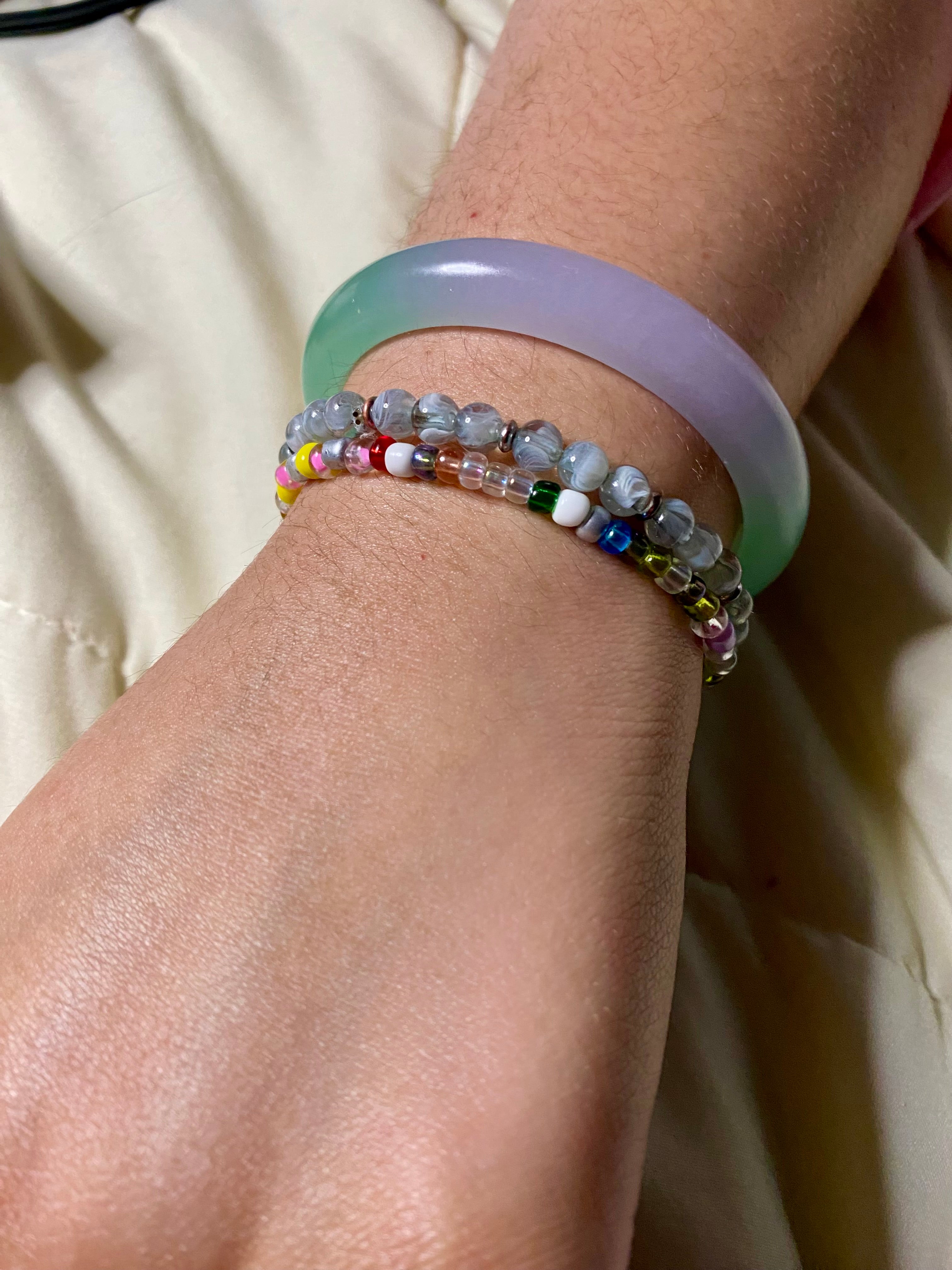 Close-up of a wrist wearing colorful stretch thick beaded bracelets on a neutral background