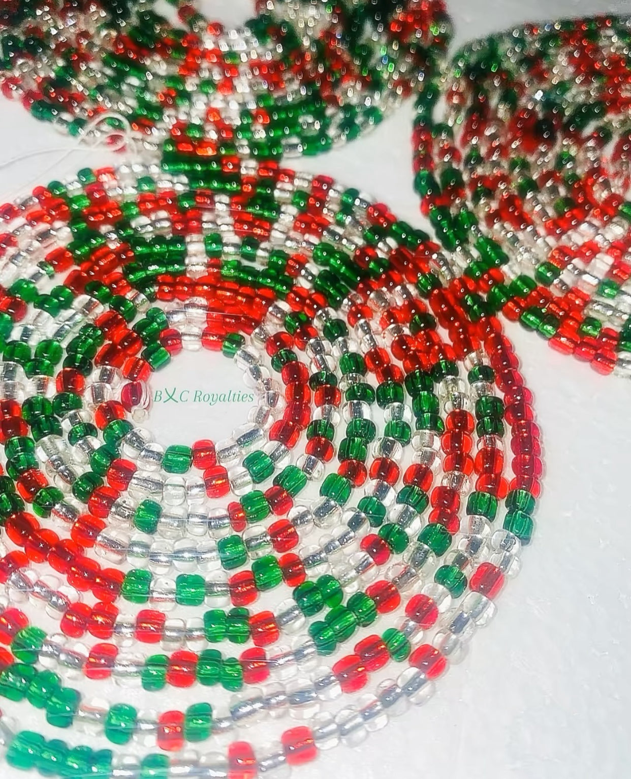 Close-up of a beaded necklace with red, green, and clear beads on a white background.