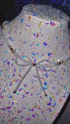 Mannequin head with colorful confetti pattern and decorative bow on a plain background